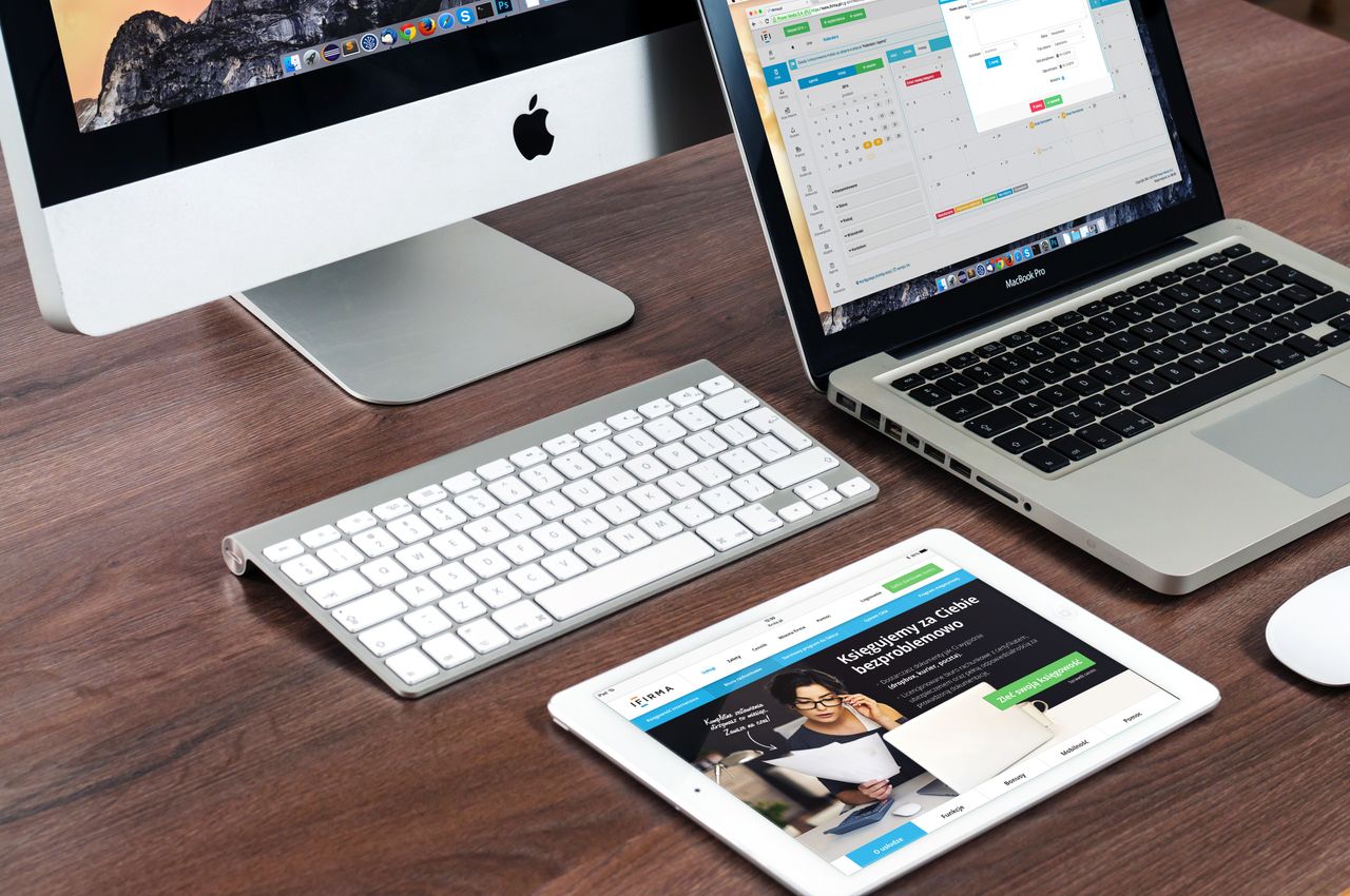 services-03 A sleek office desk setup featuring Apple devices: iMac, MacBook, and iPad.